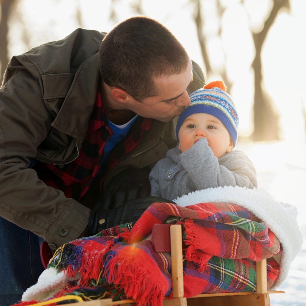 Father kissing baby boy sitting on toboggan